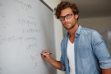 Young businessman in a suit and glasses writing on a whiteboard pointing to the work with a smile