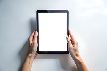 Overhead view of hands holding a modern black tablet computer with a blank white screen on a light gray surface