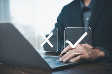 Businessman using a laptop with check mark and cross icons, symbolizing decision making, approval process, evaluation, quality control, and business choice. yes or no concept