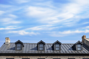 A brown metal roof with four dormer windows, stone chimneys, blue sky with clouds, sunshine, nobody