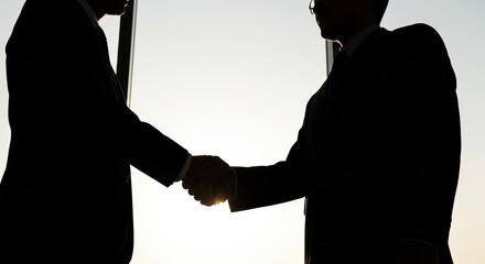 Silhouetted businessmen in suits confidently shaking hands, symbolizing trust and successful partnership against a bright, optimistic background
