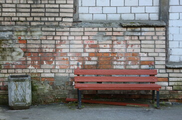 A brown wooden bench stands near an old brick wall