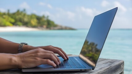 An atmospheric shot of a person's hands typing on a laptop, with a beautiful, out-of-focus tropical beach and turquoise ocean in the background.
