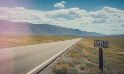 A sunlit road stretches toward distant mountains with a "Silver Creek" sign