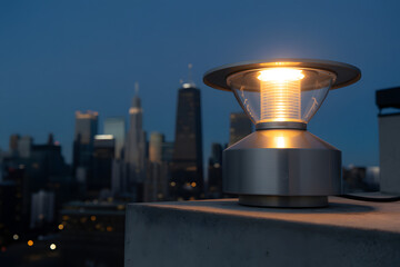 Illuminated modern outdoor lamp on rooftop with city skyline at dusk