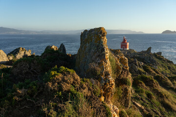 Punta Robaleira red lighthouse in Home cape at sunset in Rias Baixas zone in Galicia coast with Cíes islands in the background.
