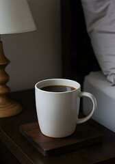 A single cup of coffee sits on a bedside table in a bedroom. A warm, inviting morning light illuminates the scene.