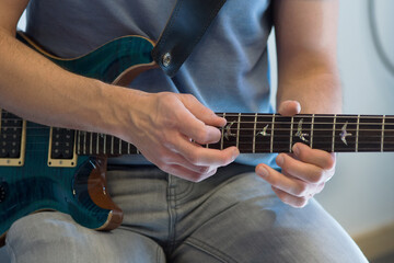 Human hand playing an electric guitar holding a chord with strings using a guitar pick
