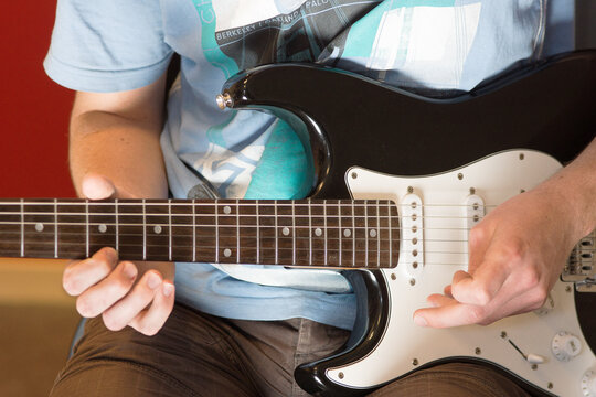 Human hand playing an electric guitar holding a chord with strings using a guitar pick