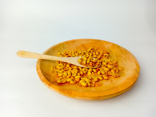 Soybeans with wooden spoon on wooden plate, isolated on white background.