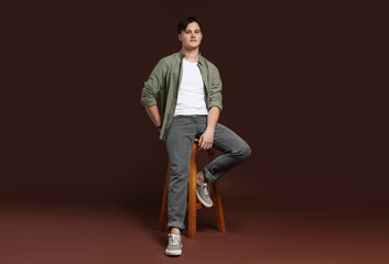 Man in stylish jeans on stool against brown background