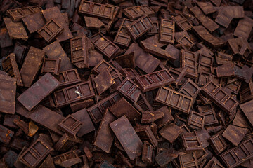 a chaotic pile of dark brown, rusted, and weathered chocolate blocks, each with intricate rectangular patterns. The blocks are scattered randomly, creating a textured, dense surface