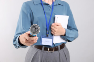 Journalist with microphone, notebook and pen on light background, closeup