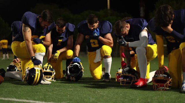 American football team kneeling in prayer before a game at night