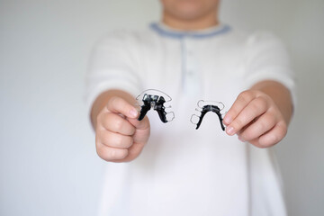 Smiling child showing two removable orthodontic retainers in hands. Dental care, orthodontics, healthy teeth and pediatric dentistry concept.
