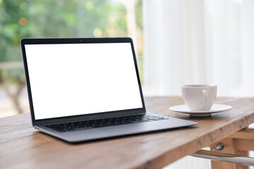 Fototapeta premium Laptop with empty white screen and cup on desk in room. Comfortable home workplace