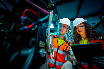 A diverse team of male and female engineers in full safety gear collaborates on machine maintenance inside a safety cage, highlighting teamwork and strict safety protocols in a factory.