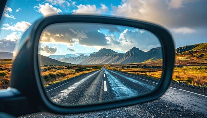 A scenic road stretches into the distance, reflected in a car's side mirror. Vast landscape of mountains and valleys under a partly cloudy sky, hinting at a journey