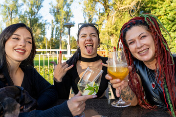 Three friends enjoying cocktails outdoors, laughing and having fun together