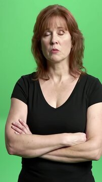 Displeased and Stern Mature Woman with Arms Crossed on Green Screen Looking at Camera with Serious Expression Conveying Disapproval and Frustration