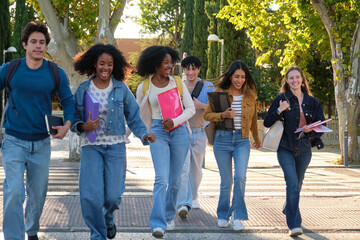Obraz premium Cheerful young adult students walking together carrying books and backpacks on a sunny day