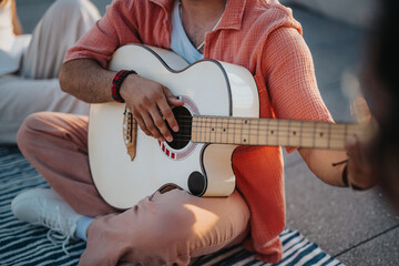 A musician strumming an acoustic guitar while relaxing with friends during a sunny outdoor rooftop...