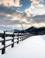 Snow-covered fence and road with cloudy sky