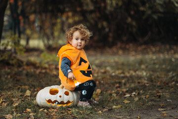 Cheerful child in pumpkin costume standing in autumn forest on Halloween.