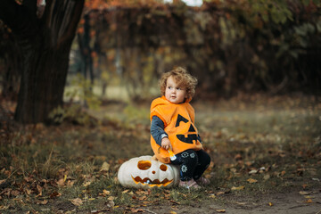 Cheerful child in pumpkin costume standing in autumn forest on Halloween.