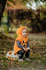 Cheerful child in pumpkin costume standing in autumn forest on Halloween.