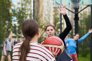 Fototapeta premium Teenage Caucasian girl holding basketball preparing to pass while another teenage Caucasian girl defending with raised arm during streetball game
