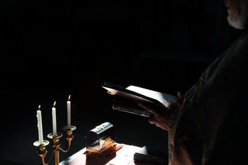 Orthodox priest reading from a holy book by candlelight during a religious ceremony in deep shadow. High quality photo