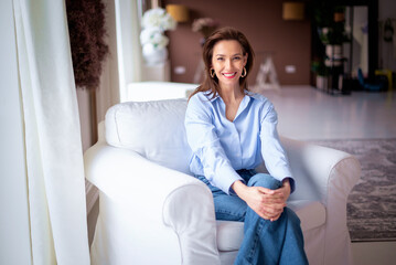 Obraz premium Portrait of a brunette haired woman relaxing in an armchair and cheerful smiling