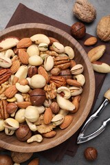 Mix of different nuts in bowl and nutcracker on grey table, flat lay