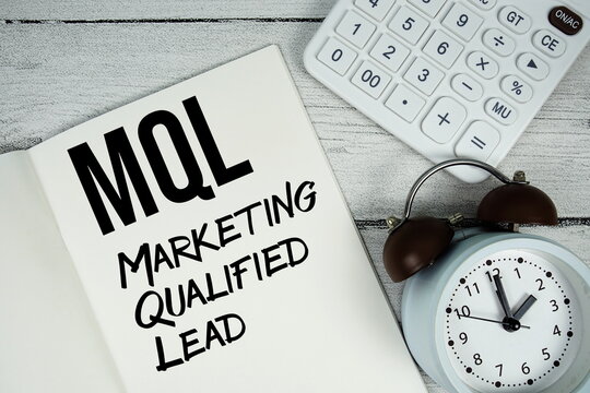 MQL Marketing Qualified Lead text on paper notebook page with alarm clock and calculator on wooden background