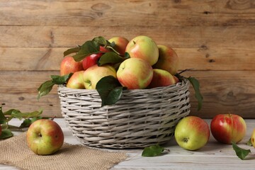 Fresh ripe apples with green leaves in wicker basket on white wooden table