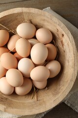 Raw chicken eggs and straw in bowl on wooden table, top view