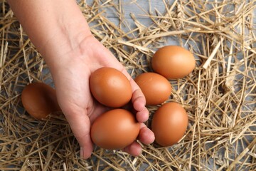Woman with raw chicken eggs and straw at grey wooden table, top view