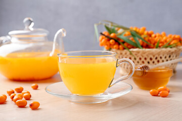 Sea buckthorn tea in glass cup, teapot, fresh berries and honey on wooden table, closeup