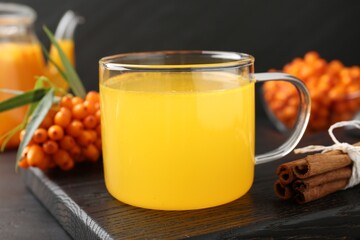 Sea buckthorn tea in glass cup, fresh berries and cinnamon on black table, closeup