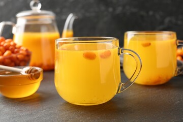 Sea buckthorn tea in glass cups, honey and fresh berries on black table, closeup