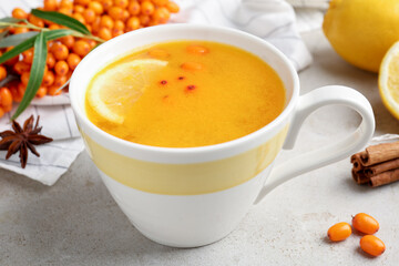 Sea buckthorn tea in cup, spices, lemon and fresh berries on light grey table, closeup
