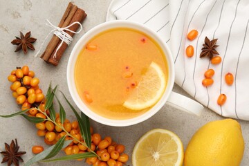 Sea buckthorn tea in cup, spices, lemon and fresh berries on light grey table, flat lay
