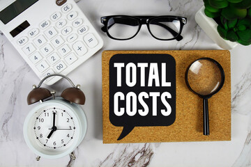 Total Costs text with Calculator, alarm clock and magnifying glass on marble background