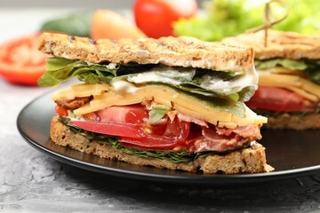 Tasty sandwiches with bacon, cheese, vegetables and sauce on grey textured table, closeup