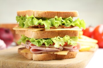 Tasty sandwich with ham, bacon, cheese and vegetables on white table, closeup