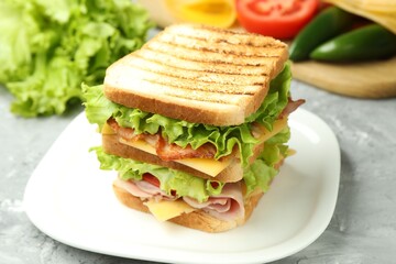 Tasty sandwich with ham, bacon, cheese and vegetables on grey textured table, closeup