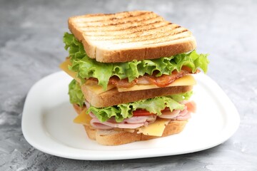 Tasty sandwich with ham, bacon, cheese and vegetables on grey textured table, closeup