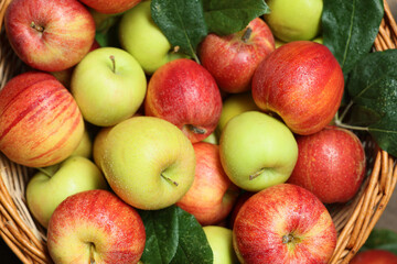 Fresh apples and green leaves in wicker basket, top view