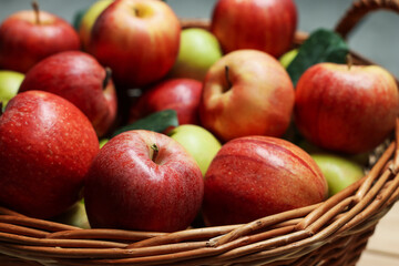 Fresh apples and green leaves in wicker basket, closeup